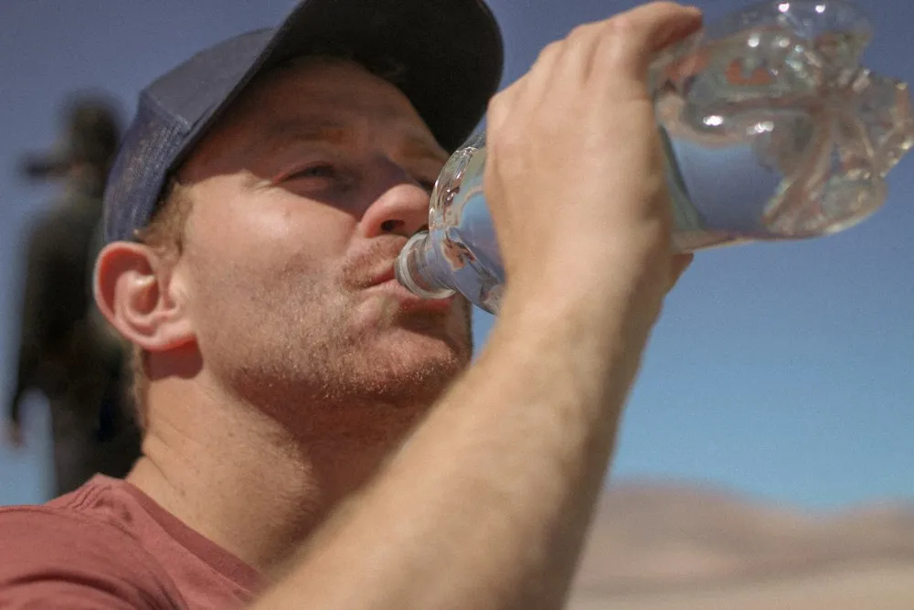 A man drinking water after a workout under a clear sky