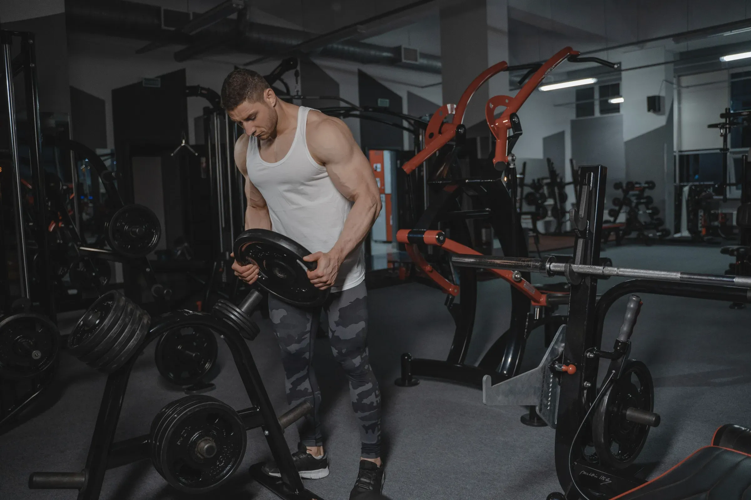 A man loading a weight plate onto a rack in a gym