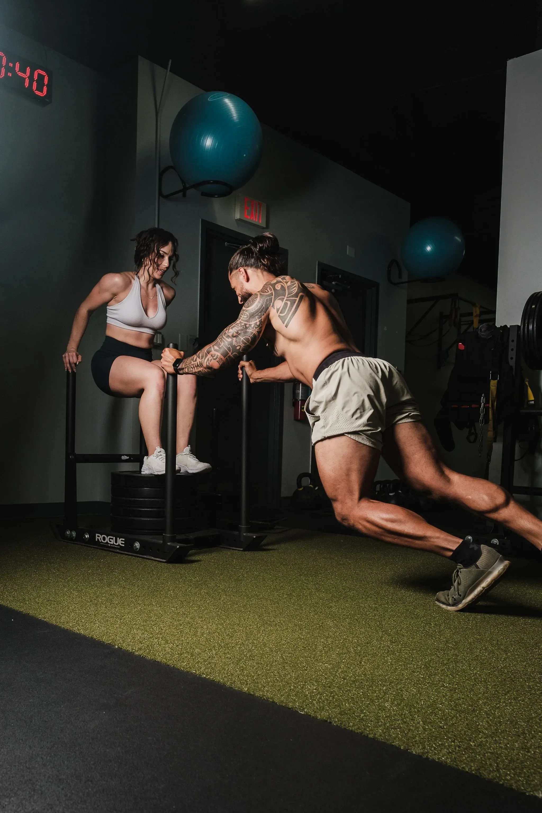 Two athletes training side by side on a turf lane in a gym