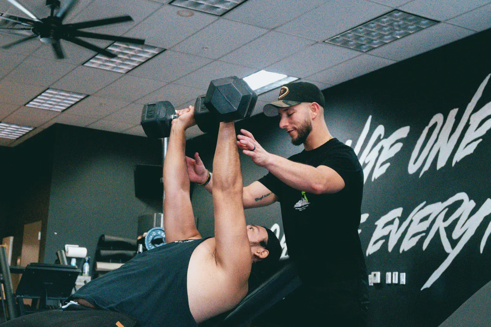 A personal trainer spotting a client through a dumbbell press